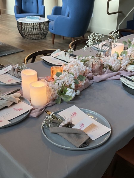 A styled event table with a pink floral runner, pillar candles, and place settings